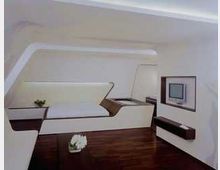 Modernes Schlafzimmer mit futuristischem Design, weißen glatten Wänden und integrierten Möbeln. Ein eingebettetes Bett, ein kleiner Wandbildschirm und dunkler Holzboden definieren den Raum.