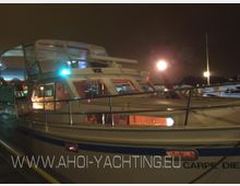 Eine beleuchtete Motorjacht mit dem Namen "Carpe Diem" liegt in einem Hafen bei Nacht. Das Schiff hat eine überdachte Flybridge, große Fenster und sichtbare Innenbeleuchtung.