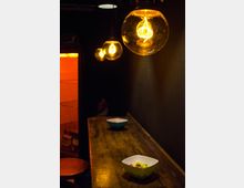 Ein dunkler Innenraum mit einer Holztheke, auf der zwei Schalen mit Snacks stehen. Über der Theke hängen mehrere runde Glühbirnen mit warmem, gelbem Licht, die den Raum sanft beleuchten.