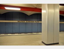 Untergrundbahnhof mit blauen Wandpaneelen, darauf der Schriftzug „Walther-Schreiber-Platz“. Eine große silberne Säule steht im Vordergrund, der Boden ist beige gefliest.