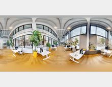 Modernes Büro mit großen, abgerundeten Fenstern, hohen Decken und Holzfußboden. Der Raum ist mit weißen Schreibtischen, Bürostühlen und zahlreichen Pflanzendekorationen ausgestattet, die ein helles und offenes Arbeitsumfeld schaffen.