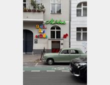 Fassade eines Altbaugebäudes mit einem Ladenlokal mit der Aufschrift „Möbel“ in grüner Leuchtschrift und einem bunten „Good Old Goods“-Schriftzug. Vor dem Gebäude sind ein grüner Oldtimer und ein schwarzes Auto auf der Straße geparkt.