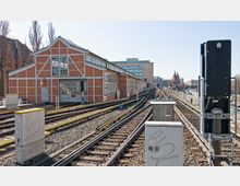 Bahnhof mit rotem Backsteingebäude und mehreren Bahngleisen, die in die Ferne führen. Im Hintergrund sind moderne und historische Gebäude sowie die Türme der Oberbaumbrücke zu sehen.