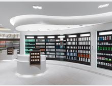 Innenansicht einer modernen Apotheke mit hell beleuchteten Regalen, die mit verschiedenen Produkten wie Flaschen und Verpackungen gefüllt sind. Im Vordergrund stehen weiße, runde Verkaufstheken mit integriertem Produktdisplay, umgeben von einem schlichten, minimalistischen Design.