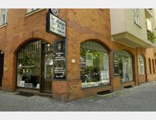 Außenansicht eines Bestattungsinstituts in einem historischen Ziegelgebäude mit großen, bogenförmigen Fenstern. In den Fenstern befinden sich Schilder mit Informationen zu den angebotenen Dienstleistungen.