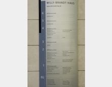 Wegweiser im Willy-Brandt-Haus mit einer Etagenübersicht der verschiedenen Büros, Organisationen und Einrichtungen, geordnet nach Stockwerken (EG bis 6). Das Schild ist vertikal ausgerichtet, mit blauer und weißer Farbgestaltung.