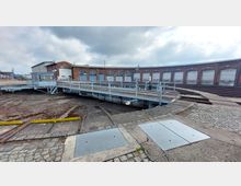 Rundlokschuppen mit einer Drehscheibe im Vordergrund. Die Backsteinfassade des Gebäudes mit hohen Toren für Lokomotiven umgibt die Drehscheibe, die mit Gleisen verbunden ist.