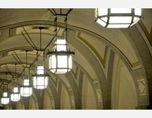 Gewölbedecke mit mehreren gleichmäßig angeordneten, achteckigen, weißen Lampen, die an Ketten von der Decke hängen. Die Decke ist mit Bögen und goldenen Zierelementen gestaltet.