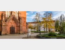 Backsteingebäude mit gotischem Spitzbogenportal und verzierten Türflügeln, flankiert von einem gepflasterten Platz mit moderner Begrünung, Bäumen und einer Informationstafel; im Hintergrund Wohngebäude.