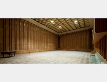 Großer, leerer Konzert- oder Proberaum mit holzvertäfelten Wänden, Parkettboden und einer Kassettendecke mit eingebauten Leuchten. Links im Raum steht ein schwarzer Flügel, rechts befinden sich gepolsterte Sitzbänke.