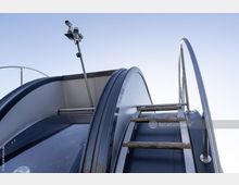 Detailansicht einer modernen Metalltreppe mit Holzstufen, Geländern aus Edelstahl und einer montierten Kamera über der Konstruktion, vor klarem Himmel.