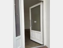 Weiße Eingangstür zu einem Geschäft oder Raum mit der Aufschrift „F26 Pop Up Store“ auf der Glasscheibe. Der Blick geht in einen leeren Raum mit weiß gestrichenen Wänden und einem Heizkörper an der hinteren Wand.