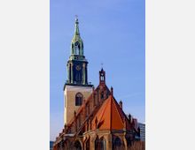 Backstein-Kirche mit spitzem, roten Ziegeldach und einem hohen Glockenturm mit grün-patinierter Kupferverkleidung. Der Himmel im Hintergrund ist klar und blau.