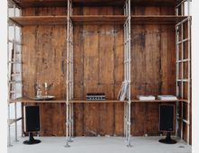 Regalwand aus Metallgerüsten und Holzpaneelen mit einer rustikalen Optik. Auf den Regalböden befinden sich ein Schallplattenspieler, Bücher, ein Tablett mit Kerzen und kleine Lautsprecher auf beiden Seiten.