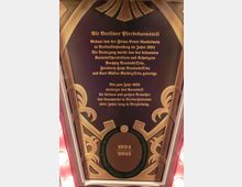 Eine dekorative Informationstafel mit geschwungenen Ornamenten und goldener Schrift, die das "Alt Berliner Pferdekarussell" beschreibt. Unten in einem Lorbeerkranz sind die Jahreszahlen 1924 und 2013 abgebildet.