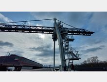 Industriegelände mit einem großen Stahlkran im Vordergrund. Im Hintergrund ist eine lange Industriehalle mit der Beschriftung "NEBRA REMINE" sowie eine freie, bewölkte Himmelsfläche zu sehen.