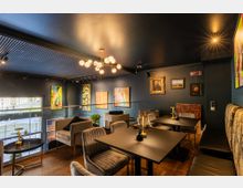 Gemütliches Café oder Lounge im Obergeschoss mit modernem und klassischem Dekor. Der Raum ist in dunklen Tönen gehalten, mit Sitzgruppen, einer Galerie aus Kunstwerken an den Wänden und großen Fenstern, die Ausblick nach draußen bieten.