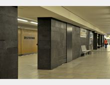 U-Bahn-Station mit dunklen Wandverkleidungen aus schwarzen Fliesen, einem gelben Wandbereich mit der Aufschrift „Ulsteinstraße“ und mehreren Sitzbänken aus Metall. Im Hintergrund ist eine Person auf dem Bahnsteig zu sehen.