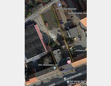 Satellitenaufnahme eines städtischen Gebiets, das von Straßen umgeben ist: Am Frauentor oben und Mönchenstraße unten. Markiert ist ein rechteckiges Grundstück mit teils bebauten und teils begrünten Flächen. In der Nähe befinden sich ein öffentlicher Parkplatz, eine Stadtbibliothek, eine DHL Packstation sowie Gewerbeeinrichtungen.