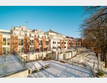 Außenansicht eines Hotels mit der Beschriftung „Inselhotel“, einem mehrstöckigen Gebäude mit roten Klinker- und weißen Fassadenteilen. Im Vordergrund sind eine verschneite Terrasse mit Geländern und Bäume zu sehen.