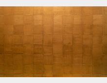 Wand mit gleichmäßig angeordnetem, rechteckigem Muster aus quadratischen Feldern in einem goldbraunen Farbton. Die Oberfläche wirkt texturiert und leicht reflektierend.