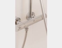 Nahaufnahme einer modernen glänzenden Duscharmatur aus Chrom mit Handbrause an einer Wand in einem Badezimmer. Die Einstellungsknöpfe und der Duschschlauch sind sichtbar, vor einem weißen, gefliesten Hintergrund.