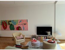 Wohnzimmer mit hellem Holzboden, einer großen abstrakten Wandmalerei in Pink- und Grüntönen, einem Fernseher auf einem schlichten weißen Regal mit Büchern und Dekoration sowie einer Sitzecke mit Sesseln, einem Couchtisch und Blumenvasen. Rechts steht eine weiße Stehlampe in modernem Design.