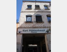 Fassade eines mehrstöckigen, weiß gestrichenen Backsteingebäudes mit Sprossenfenstern und dekorativen Ziegelbändern. Über einer breiten Durchfahrt hängt ein Schild mit der Aufschrift „Kurt Mühlenhaupt Museum“.
