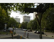 Straßenszene mit beschilderter Kreuzung "Hanseatenweg" und "Bartningallee", umgeben von Bäumen sowie parkenden Autos am Straßenrand. Im Hintergrund sind mehrstöckige Wohngebäude sichtbar, teils vor bedecktem Himmel.