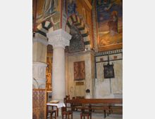 Innenraum einer historischen Kirche mit kunstvoll bemalten Wänden und Decken. Zu sehen sind Säulen mit verzierten Kapitellen, eine Kanzel, Holzbänke sowie religiöse Wandgemälde und Steinreliefs.