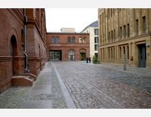 Pflastersteinerne Gasse inmitten eines historischen Backstein-Ensembles mit Arkaden im Bereich der Kulturbrauerei. Im Hintergrund ein Gebäude mit der Aufschrift „Kino in der Kulturbrauerei“, flankiert von gelblichen und roten Ziegelbauten.