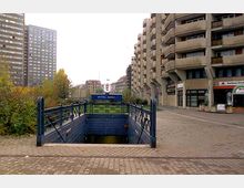 Eingang zur U-Bahn-Station "Spittelmarkt" in Berlin, umgeben von modernen Wohn- und Geschäftsgebäuden aus Beton. Im Hintergrund sind Bäume und weitere Gebäude sichtbar.