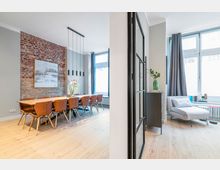 Heller, moderner Wohn- und Essbereich mit freiliegender Backsteinwand, langem Holzesstisch mit mehreren Stühlen und schlichten Hängeleuchten. Rechts daneben eine Sitzecke mit grauer Chaiselongue vor großen Fenstern mit Vorhängen, getrennt durch eine schwarze Glastür im Industriestil.