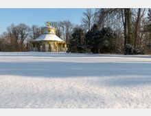 Pavillon in chinesischem Stil mit runder Kuppel und goldenen Verzierungen, umgeben von schneebedeckter Landschaft und kahlen Bäumen an einem sonnigen Wintertag.
