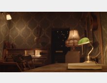 Ein gemütlicher Raum mit gedämpfter Beleuchtung, einer antiken Tapete mit Ornamentmuster, einem Klavier im Hintergrund und einer Tischlampe mit grünem Schirm auf einem Holztisch neben einem aufgeschlagenen Buch. Im Hintergrund sind ein Leuchtschalter sowie ein dimm beleuchteter Türbereich mit kleinen Lichtern erkennbar.