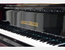 Nahaufnahme eines glänzend schwarzen Klaviers der Marke "August Förster" mit sichtbarer Tastatur und goldener Markenschrift auf der Klavierfront.
