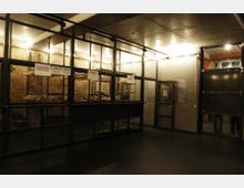 Industriell gestaltete Garderobe in einem Innenraum mit Metallgittern und Kleiderbügeln auf Kleiderstangen. Die Umgebung ist schlicht gehalten mit Betonwänden und gedämpfter Beleuchtung.