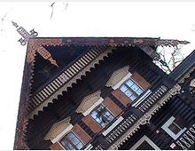 Holzhaus im russischen Baustil mit detaillierten Schnitzereien an Dach und Fensterrahmen. Das spitz zulaufende Dach ist mit ornamentalen Verzierungen geschmückt.