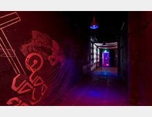 Dunkler Flur mit roten und violetten Lichteffekten, Wandgraffiti auf der linken Seite und einer beleuchteten Tür am Ende des Gangs, durch die grünes Licht sichtbar ist. Die Decke ist mit hängenden Lampen ausgestattet, und auf der rechten Wand befinden sich projizierte Zahlen.