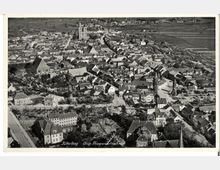 Luftaufnahme der Stadt Jüterbog mit dicht bebautem historischen Stadtkern, bestehend aus Häusern mit Satteldächern. Im Hintergrund sind große Kirchen und Wehrtürme zu sehen, umgeben von Feldern und ländlicher Landschaft.