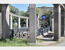 Steinbogenkonstruktion mit verzierenden Metallgeländern an einem U-Bahn-Eingang mit blauer Beschilderung „Heidelberger Platz“. Im Hintergrund stehen Bäume und ein mehrstöckiges Wohngebäude.