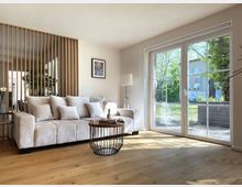 Wohnzimmer mit heller Einrichtung, bestehend aus einem beigefarbenen Sofa mit vielen Kissen, einem runden Couchtisch mit Metallgestell und großen Fenstern, die Licht hereinlassen und den Blick auf einen grünen Außenbereich ermöglichen. Im Hintergrund trennt eine Holzlamellen-Wand den Wohnbereich optisch vom Rest des Raumes.