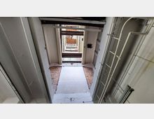 Blick in einen mehrstöckigen Gebäudekern mit freigelegten, teils sichtbaren Backstein- und weißen Fliesenwänden. Metallgerüste und Rohre sind an den Wänden befestigt, sowie offene Decken- und Bodenstrukturen erkennbar.