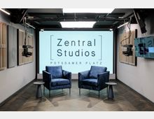 Moderner Studio-Raum mit zwei blauen Sesseln und kleinen Beistelltischen vor einer großen weißen Wand mit der Aufschrift „Zentral Studios Potsdamer Platz“. An den Seiten befinden sich schallabsorbierende Elemente, Kameras und Beleuchtung sind an der Decke montiert.