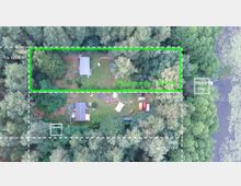 Luftaufnahme eines Waldgrundstücks mit klar markierten Bereichen. Sichtbar sind Gebäude, eine Sauna, ein Bootssteg am Rand eines Gewässers und Freiflächen mit Tischen und Fahrzeugen, umgeben von dichtem Baumbestand. Die Gesamtfläche ist in Abschnitte von ca. 2.000–6.000 m² unterteilt.