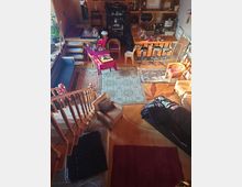 Wohnraum mit offener Gestaltung, Holzboden und verschiedenen Ebenen. Die Einrichtung umfasst einen Esstisch mit Stühlen, eine Sitzecke mit Sesseln und Sofas, Teppiche und eine hölzerne Treppe, die zu einem erhöhten Bereich führt.