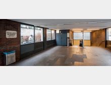 Eingangsbereich einer U-Bahn-Station mit Treppen und Rolltreppen, umgeben von Ziegelwänden und Fenstern, die nach draußen blicken. Links ist ein Mülleimer und ein Hinweisschild mit der Aufschrift „Fahrräder abstellen und anschließen untersagt!“.