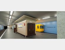 U-Bahn-Station mit grauem Boden und blauen Kacheln an den Wänden. Ein gelber Zug fährt auf der rechten Seite ein, während ein zentraler Bereich mit beigen Fliesen, einer Beschilderung "Afrikanische Straße" und einer kleinen Eingangsstruktur sichtbar ist.