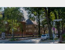 Straßenansicht einer Wohngegend mit mehrstöckigen, hellbraunen Häusern, die teilweise von Bäumen verdeckt sind. Im Vordergrund liegt die gepflasterte Straße mit parkenden Autos, einem Straßenschild "Finckensteinallee" und einem Verkehrsschild für Tempo-30-Zone.