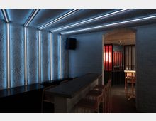 Kleiner moderner Innenraum einer Bar mit Betonwänden, schmalen LED-Leuchtstreifen an der Decke und den Wänden, einer Stein-Theke mit Barhockern und einem Durchgang zu einem Bereich mit roten und schwarzen Gitterelementen. Die Atmosphäre ist durch gedämpftes Licht geprägt.
